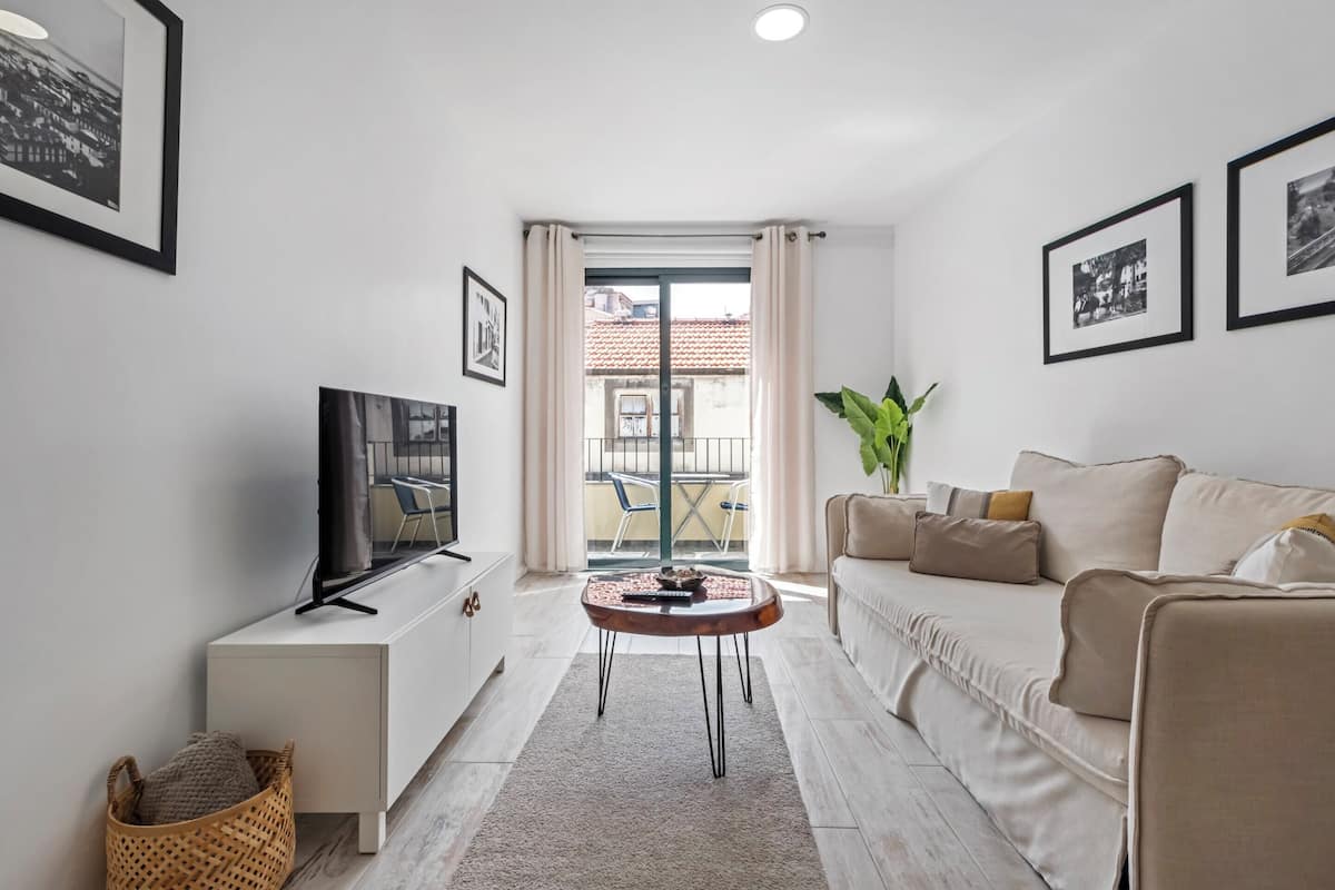 Una sala de estar moderna con una televisión de pantalla plana, un sofá, una mesa de centro y un balcón con vistas a edificios.