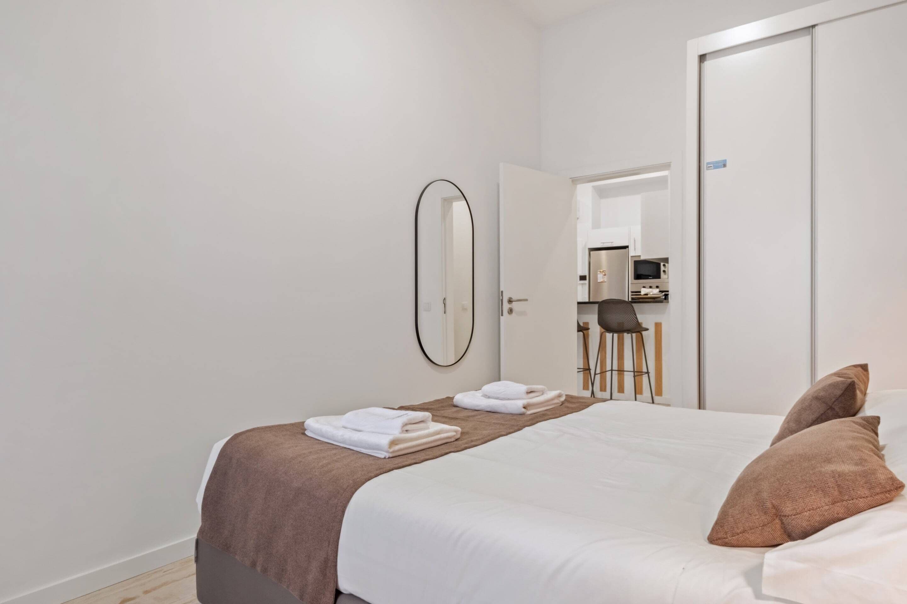 A hotel room with a bed, a mirror, and a door leading to a bathroom.