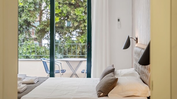 A hotel room with a bed, pillows, a bedside lamp, and a view of a balcony with a table and chairs. - Tanoeiros Residence by An Island Apart (Funchal)