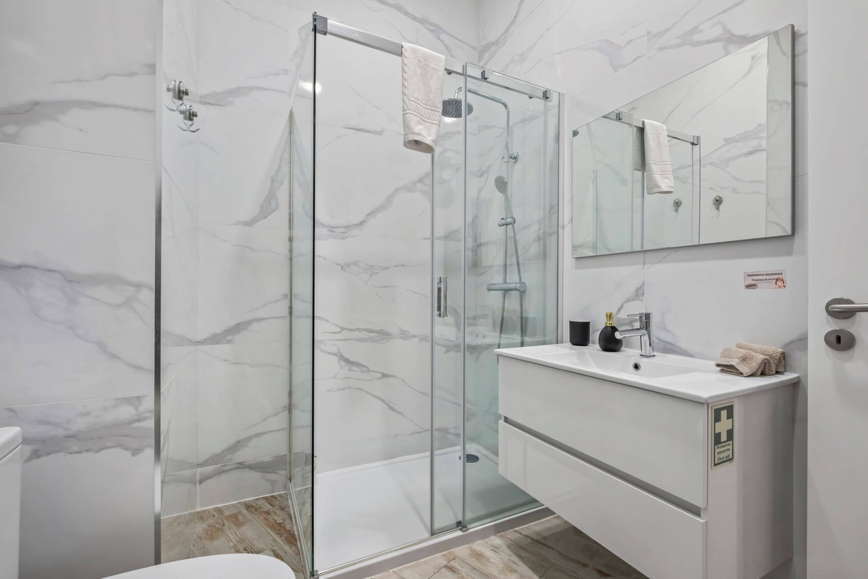 A modern bathroom with a glass-enclosed shower, a white sink, and a large mirror.
