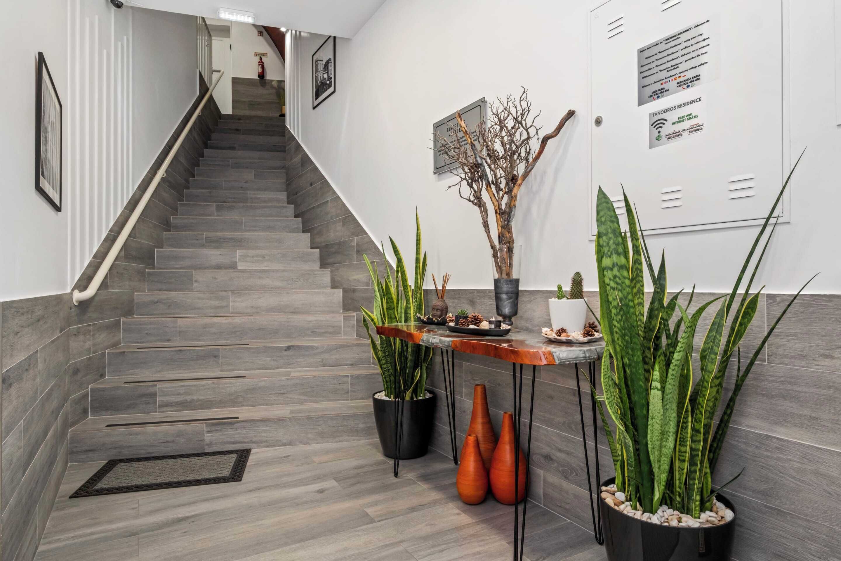 A modern hotel lobby with a staircase, potted plants, and a reception desk.