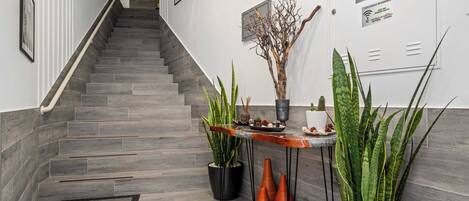 A modern hotel lobby with a staircase, potted plants, and a reception desk.