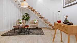 A modern living room with a wooden staircase, a sofa, a coffee table, and a small side table with decorative items. - Tanoeiros Residence by An Island Apart (Funchal)