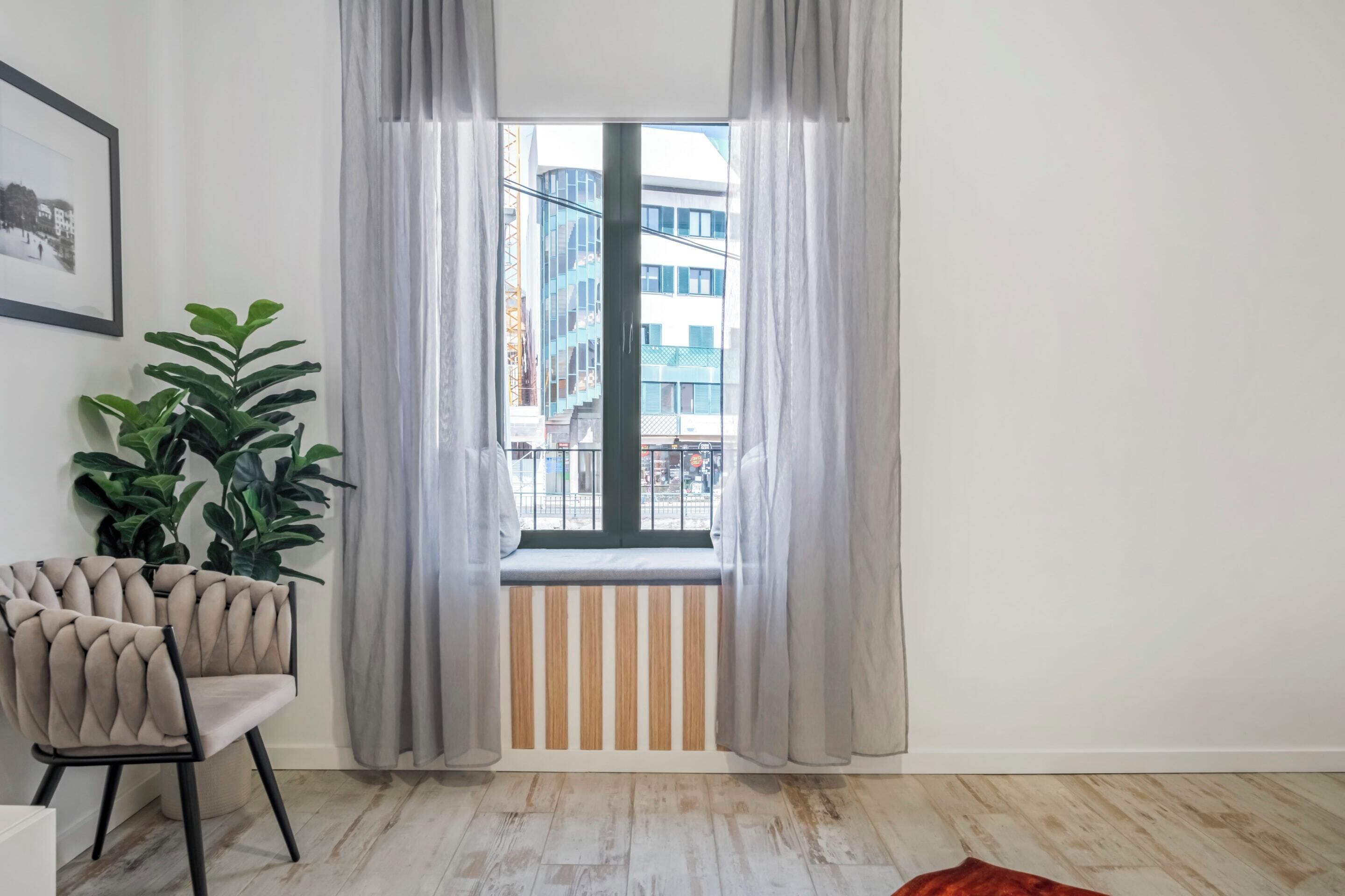 Een kamer met een raam, een kamerplant en een stoel.