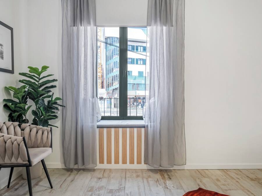 Een kamer met een raam, een kamerplant en een stoel.