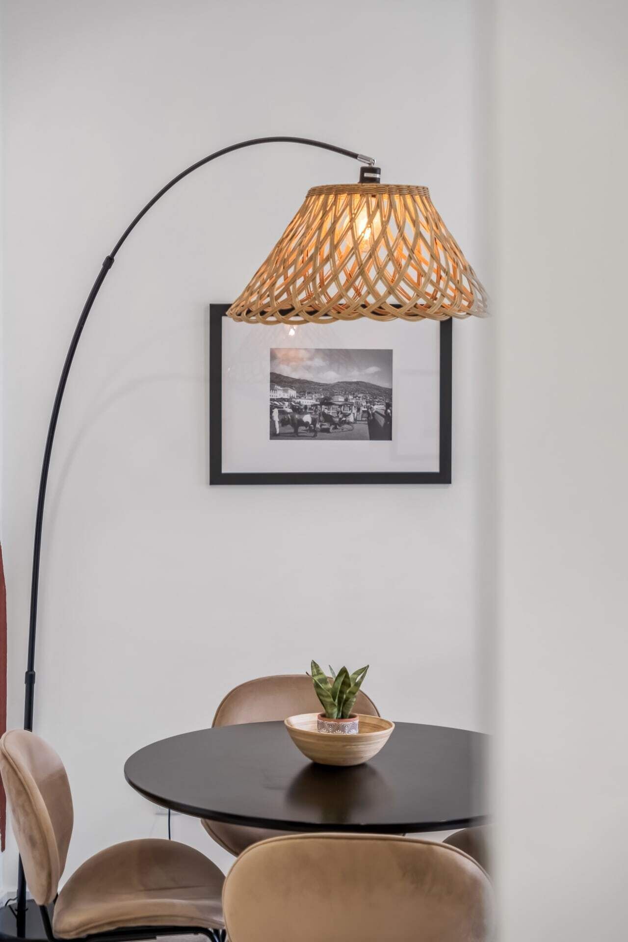 Habitació moderna amb una taula rodona, una fotografia en blanc i negre emmarcada, una làmpada de vimet i una petita planta en test.