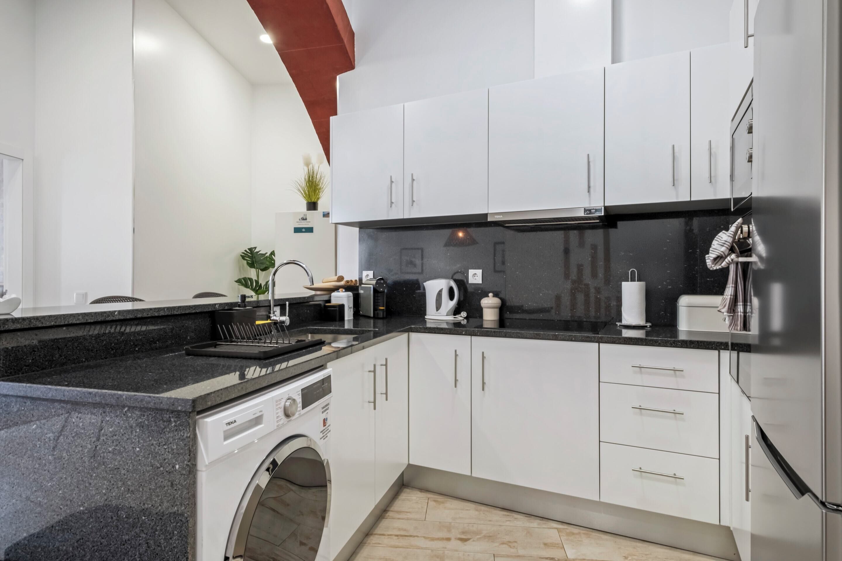 Une cuisine moderne avec des meubles blancs, un plan de travail noir et un lave-linge encastré.