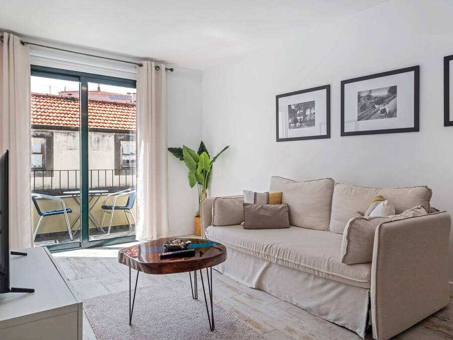 Ein modernes Wohnzimmer mit einer Couch, einem Couchtisch und einem großen Fenster mit Vorhängen. An der Wand hängen zwei gerahmte Bilder.