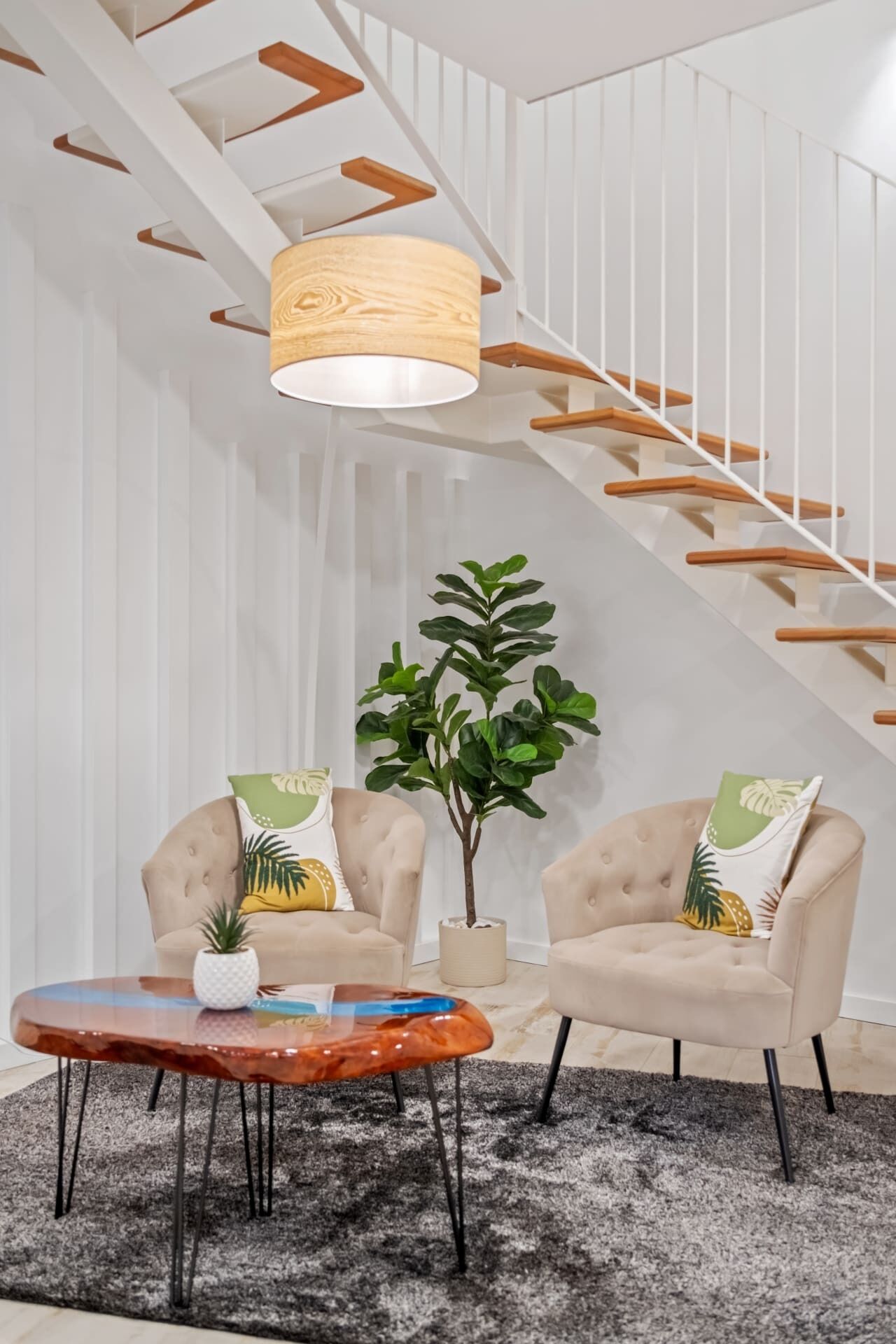 A modern living room with a staircase, two armchairs, a coffee table, and a potted plant.