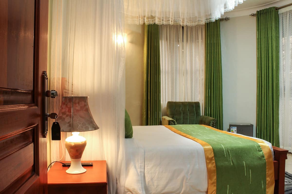 A hotel room with a bed, a chair, a desk, a lamp, and curtains.