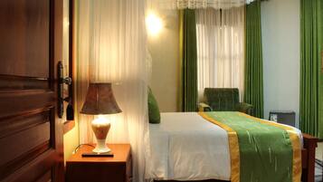 Una habitación de hotel con una cama, una mesita de noche con lámpara, una silla y un escritorio con ordenador.