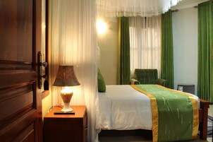 Una habitación de hotel con una cama, una mesita de noche con lámpara, una silla y un escritorio con ordenador.