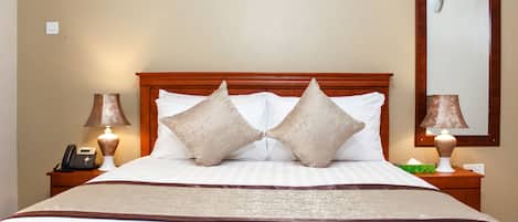 Una cama bien hecha con cabecera de madera, dos lámparas de noche, un teléfono y un espejo en la pared.