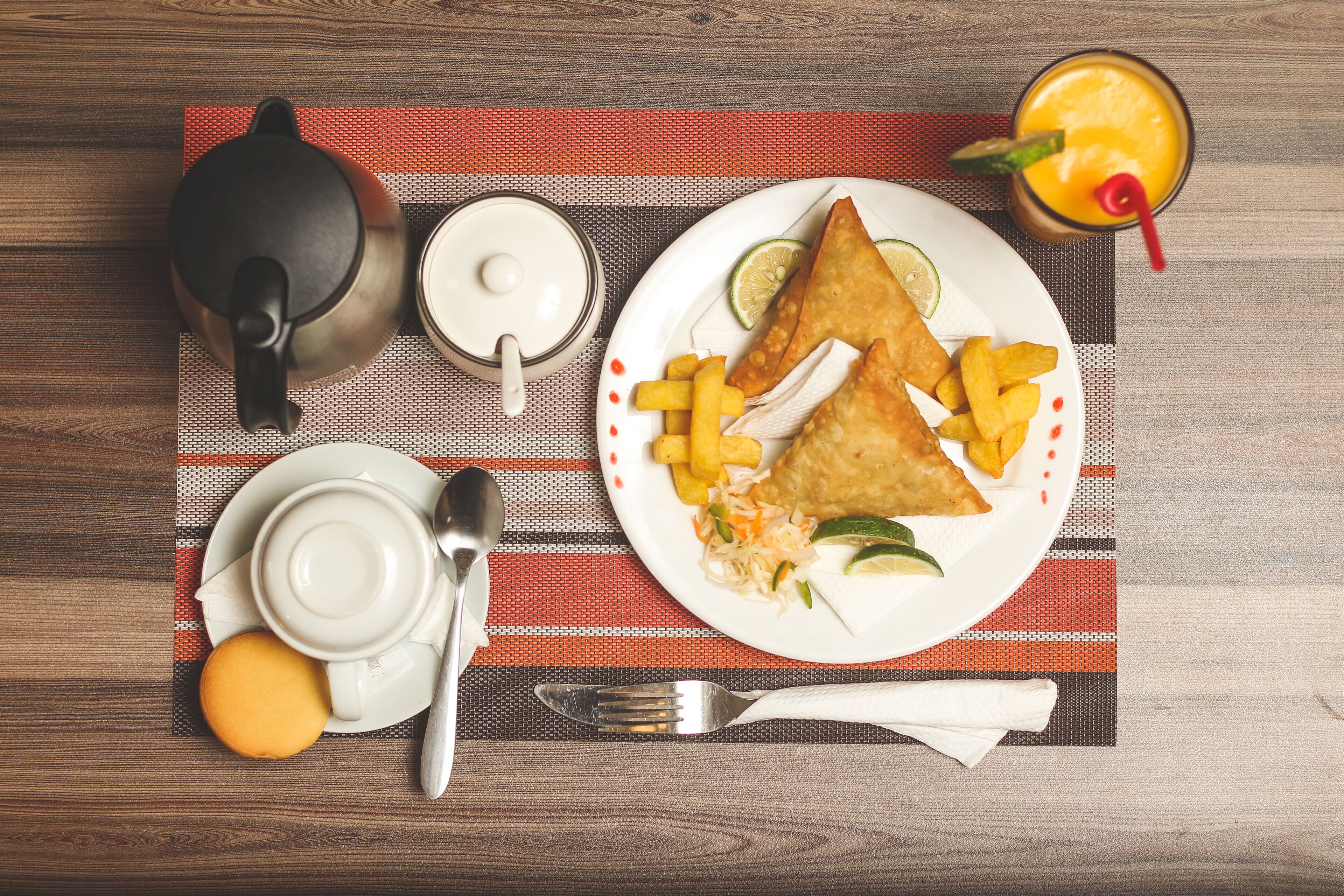 Un desayuno con un plato de comida, una tetera, una taza y un vaso de jugo de naranja sobre una servilleta.