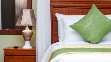A neatly made bed with a green pillow and a white pillow, a bedside lamp on a wooden nightstand, and a remote control on the nightstand.