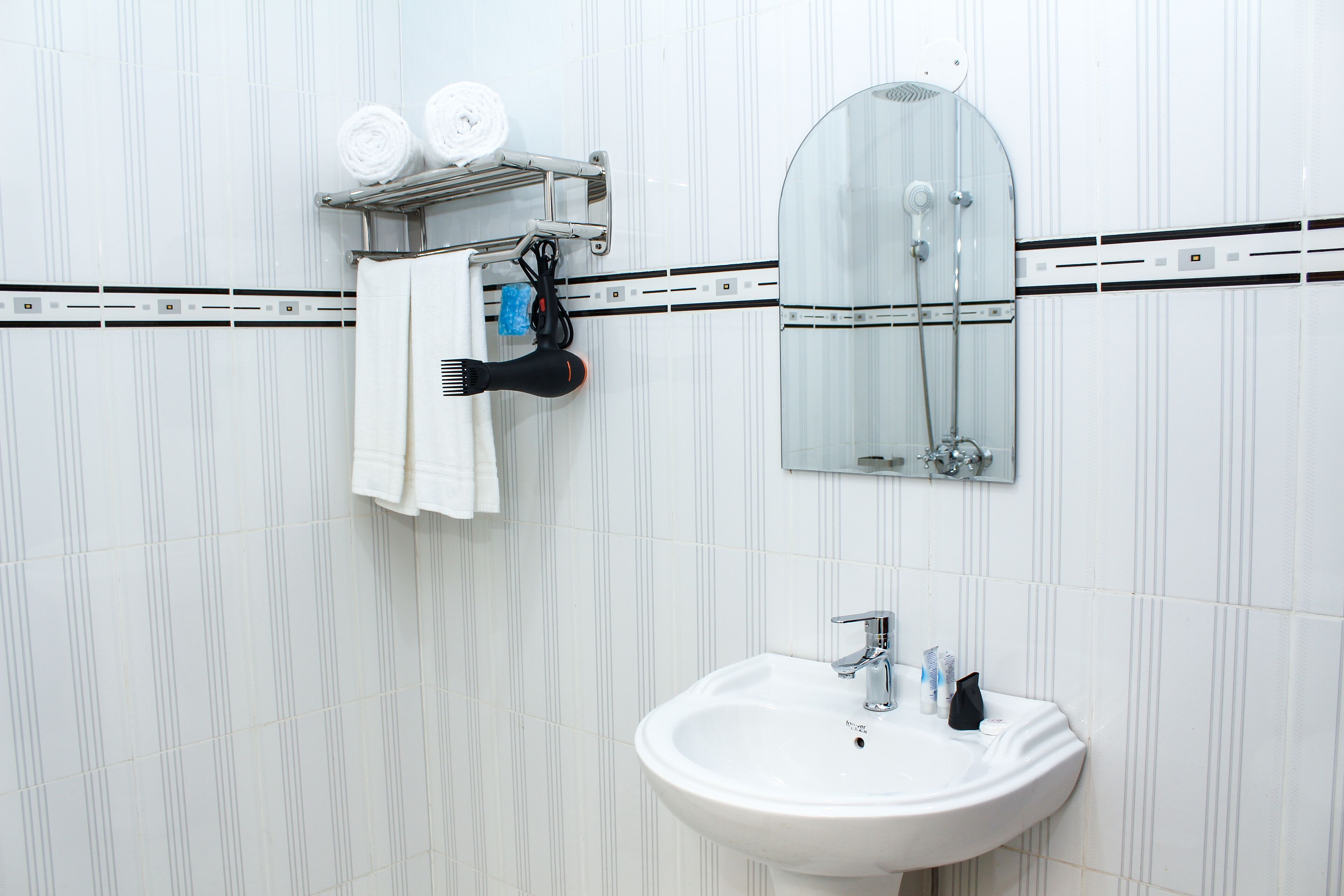 A bathroom with a white sink, a mirror, and a towel rack with towels.