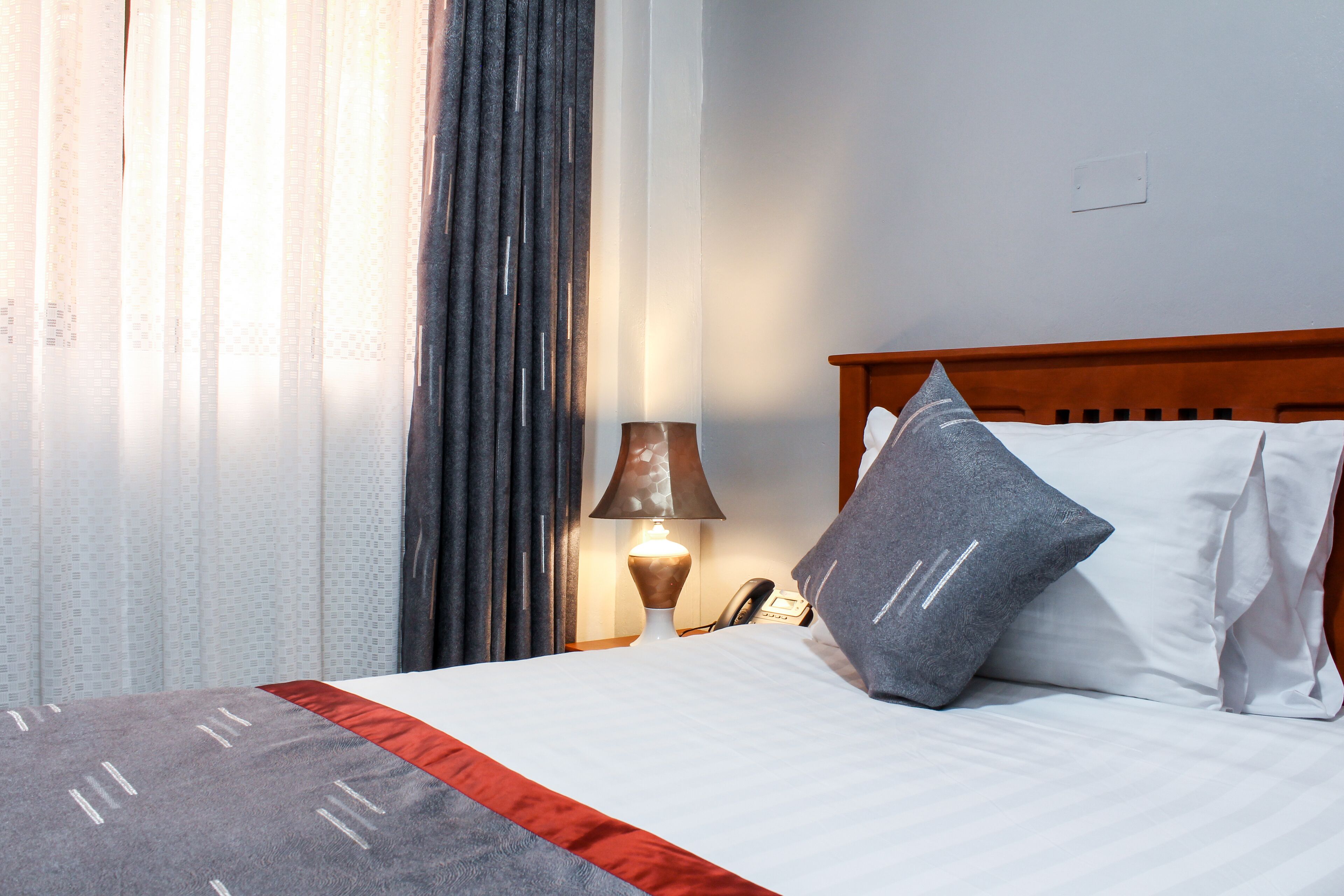 A neatly made bed with a red and white bedspread, a lamp, and a telephone on a wooden nightstand.