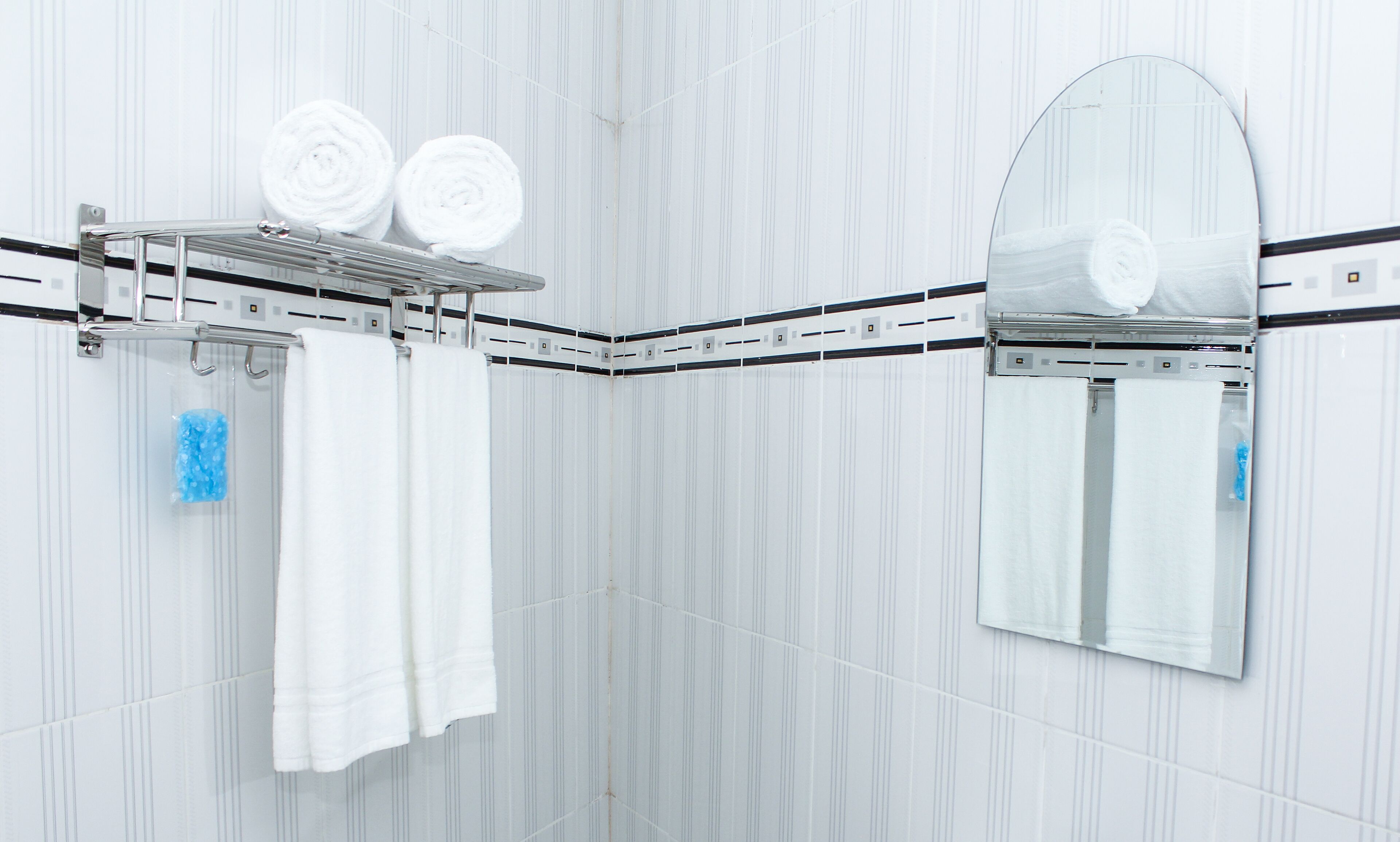 A bathroom with a white tiled wall, a towel rack with two towels, a blue soap dispenser, and a mirror.