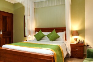 Una cama bien tendida con una colcha verde y blanca, dos almohadas verdes y un cabecero de madera.