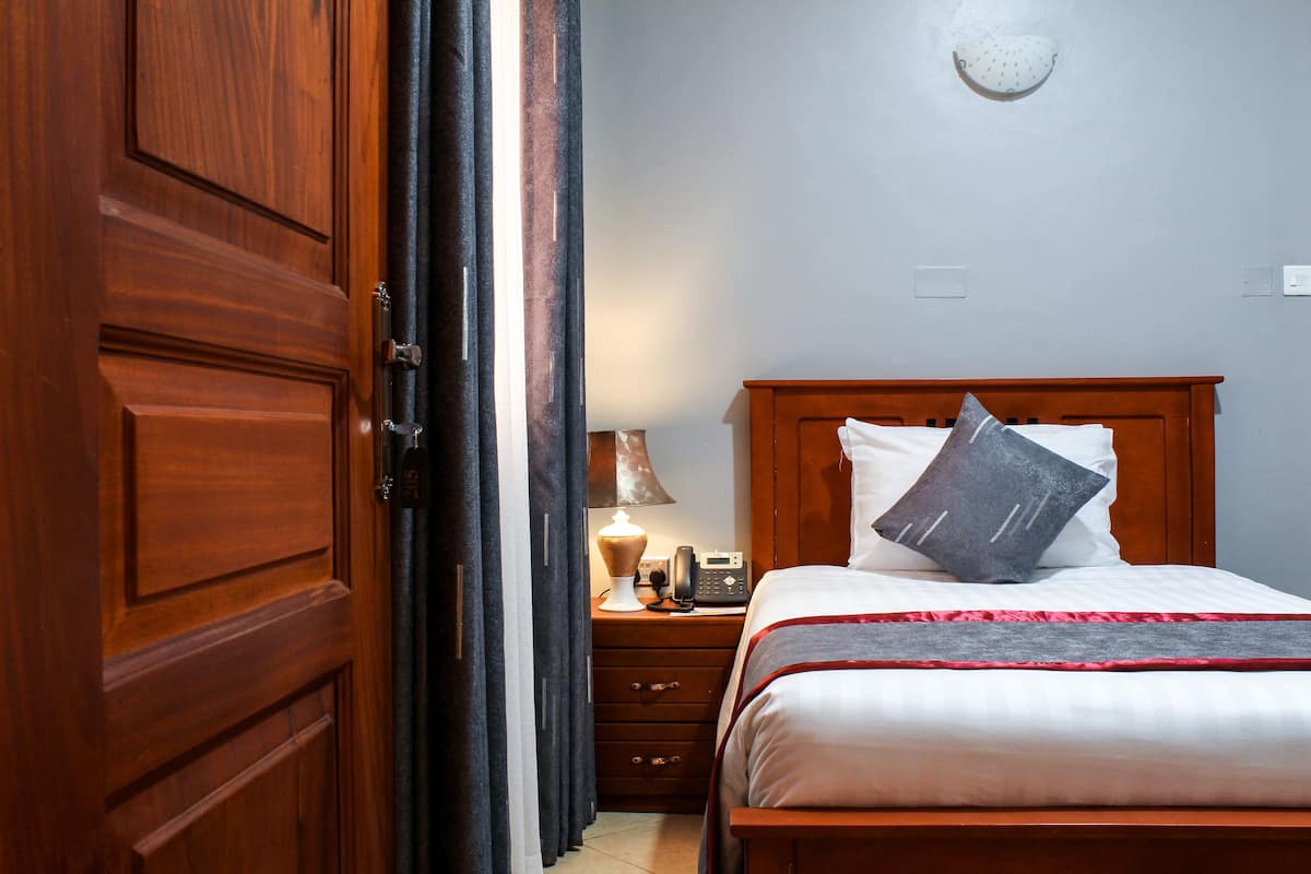 A hotel room with a wooden bed, a nightstand with a lamp, and a wardrobe.