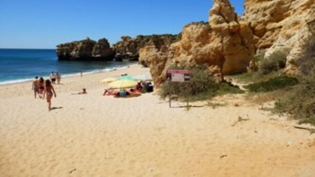 A beach with rocky cliffs, a sandy shore, and a few umbrellas.