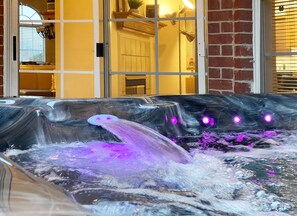 Ein Whirlpool mit Wasserstrahlen und violetter Beleuchtung, vor einer Ziegelwand und einem Fenster mit Jalousien.