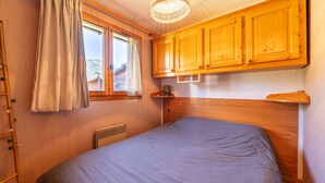 A bedroom with a bed, wooden cabinets, a window with curtains, and a radiator. - Wonderful apt 6 ppl with terrace (Morillon)