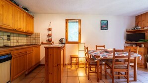 A kitchen with wooden cabinets, a tiled backsplash, a dining table with chairs, a window with blinds, and a poster on the wall. - Wonderful apt 6 ppl with terrace (Morillon)