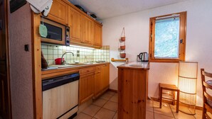 A compact kitchen with wooden cabinets, a dishwasher, a microwave, and a window with blinds. - Wonderful apt 6 ppl with terrace (Morillon)