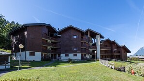 A multi-story wooden building with balconies, a central staircase, and a mountain backdrop. - Wonderful apt 6 ppl with terrace (Morillon)