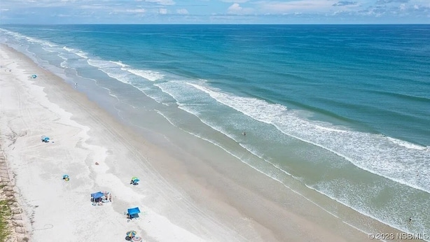 Ein Strand mit blauem Himmel, ruhiger Wellen und mehreren Sonnenschirmen.