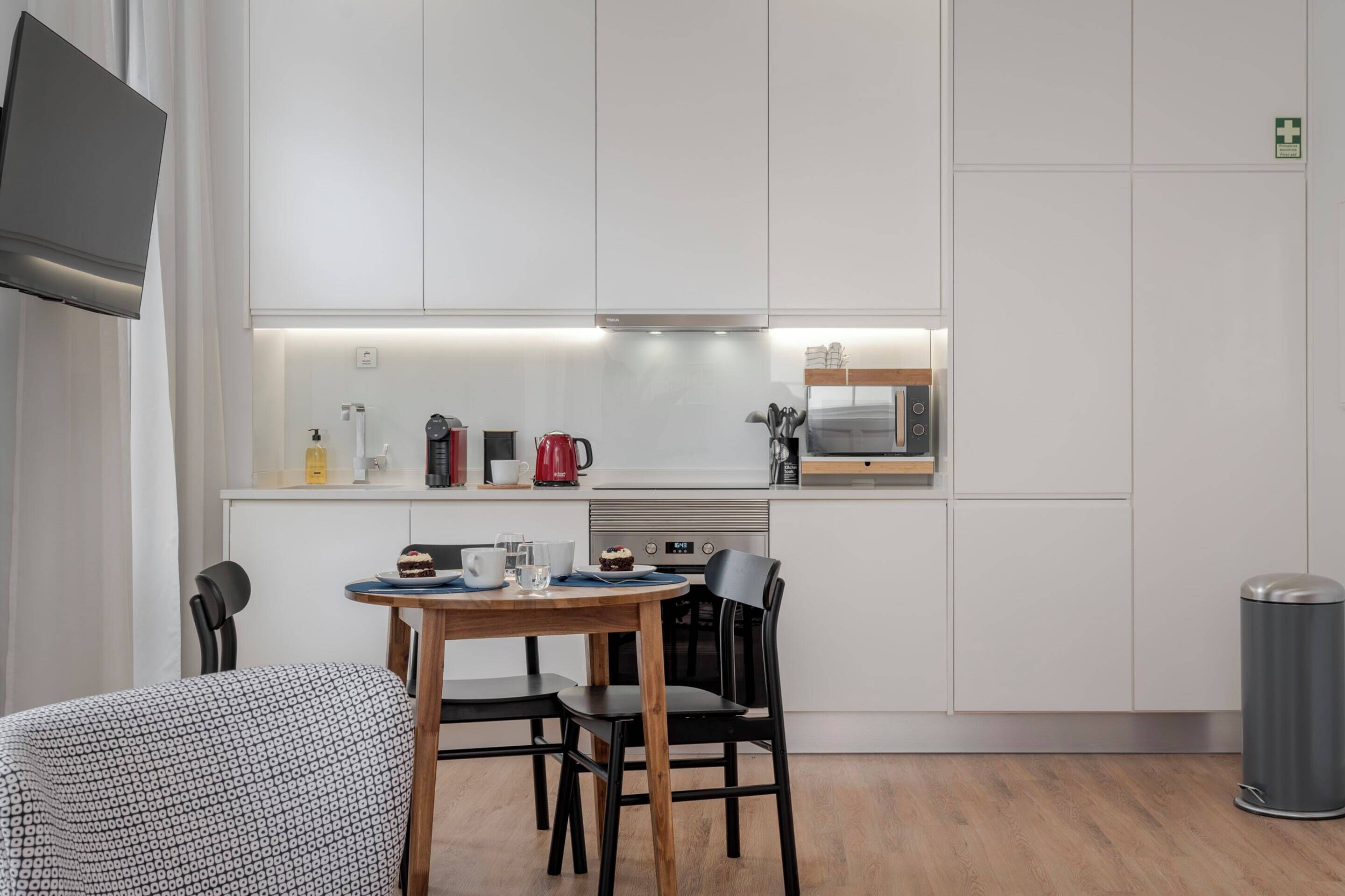 A modern kitchen with white cabinets, a wooden dining table, and a black trash bin.