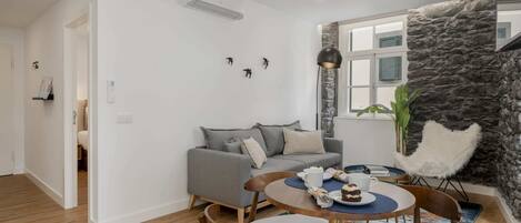 A modern living room with a grey sofa, a round dining table with chairs, a stone accent wall, and a white ceiling.