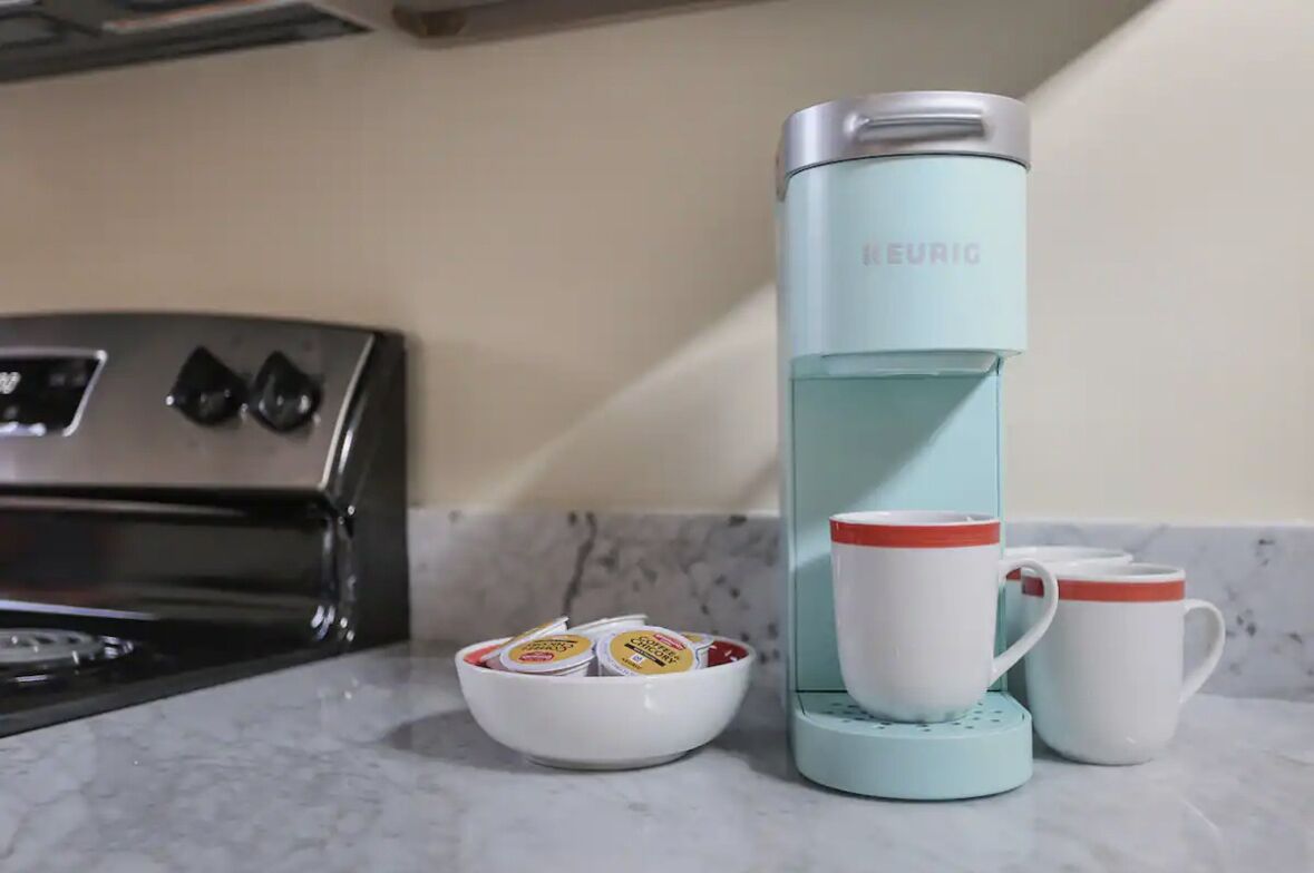 Une cuisine équipée d’une machine à café, d’un récipient contenant des capsules de café et de deux tasses.