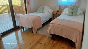 A bedroom with two beds, a wooden floor, and a balcony. - Spacious 2 or 3 BR ocean side home with pool - private lot & panoramic views. (Utila)