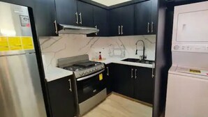 Una cocina compacta con armarios oscuros, un refrigerador de acero inoxidable, una estufa y un microondas.