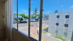 Una habitación con un amplio ventanal con vistas a una calle bordeada de palmeras y un cielo azul despejado.