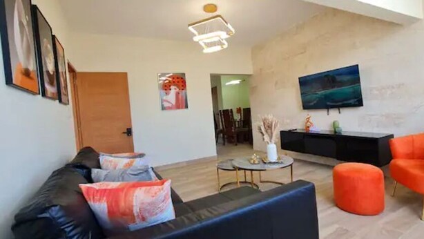 Una sala de estar moderna con un sofá negro, un sillón naranja y una mesa de centro redonda.