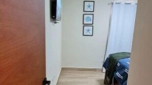Un estrecho pasillo con piso de madera que conduce a una habitación con una cama y una ventana con cortinas.