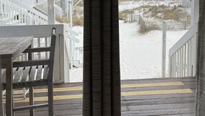 A view from a balcony with a wooden deck, overlooking a sandy beach and a wooden fence.