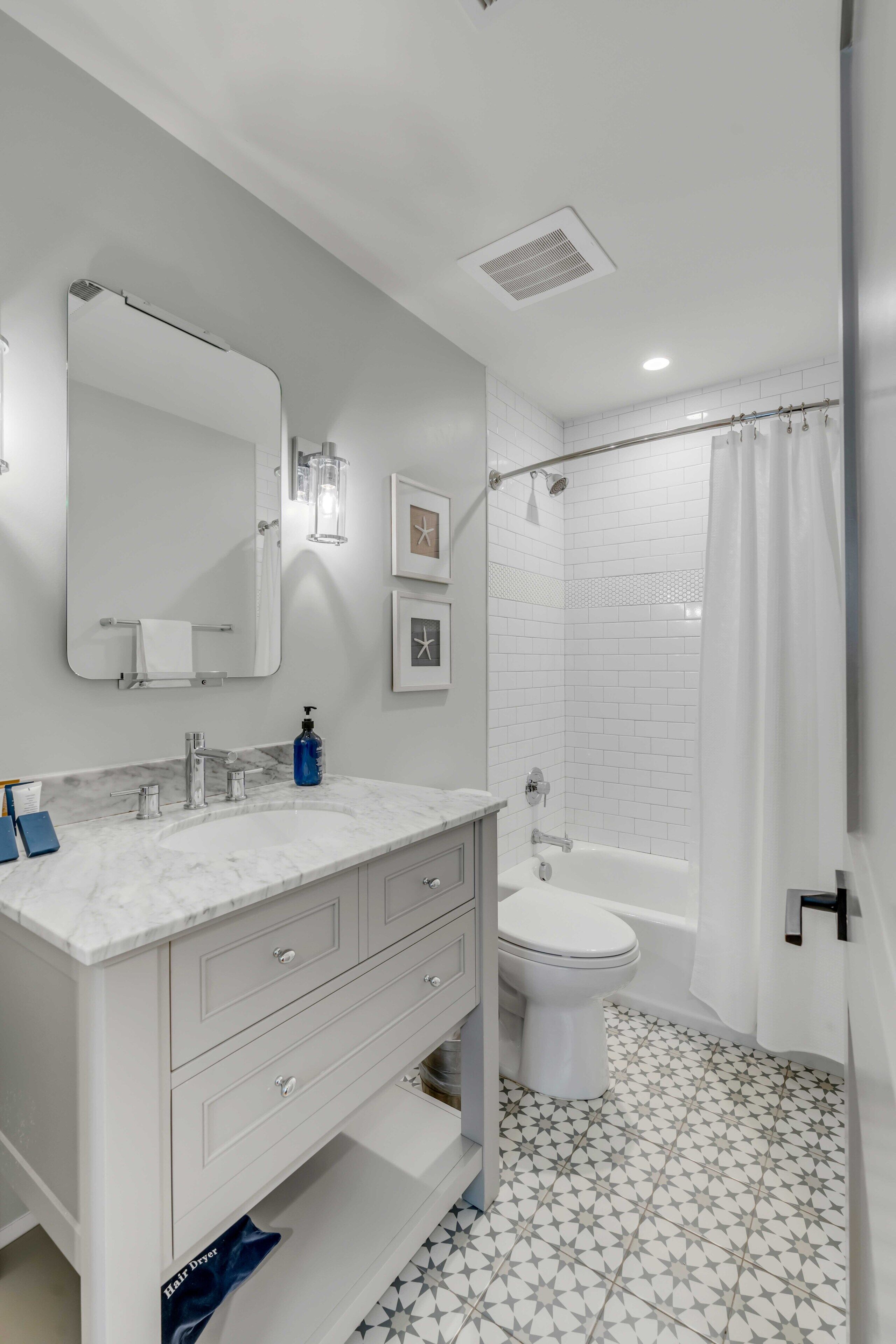 A modern bathroom with a marble vanity, a toilet, a shower with a curtain, and a tiled floor.
