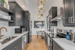 A modern kitchen with dark cabinetry, stainless steel appliances, a white countertop, and a central island. - The Palmetto House (Charleston)