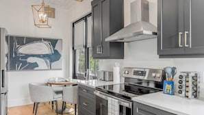 Een moderne keuken met donkergrijze kastjes, een roestvrijstalen fornuis en een houten vloer. Er hangen twee hanglampen met een geometrisch ontwerp.