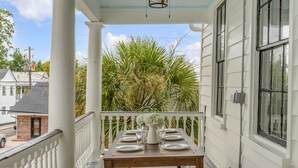 Een veranda met een tafel voor vier personen, omringd door witte hekken en uitzicht op een weelderige tuin.
