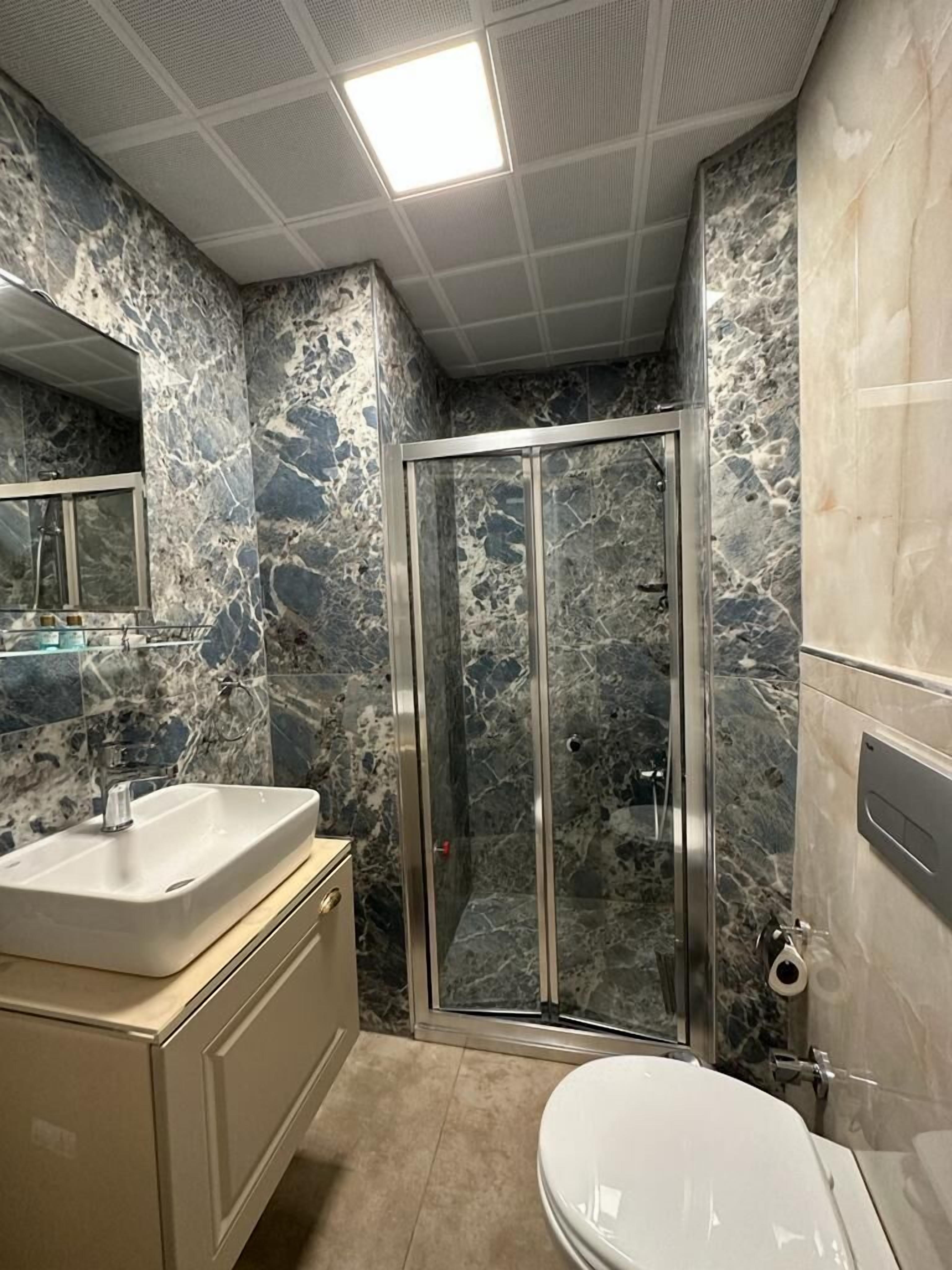 Un baño con pared de mármol, cabina de ducha de vidrio, lavabo e inodoro.