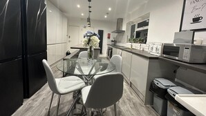 Une cuisine moderne avec une table à manger en verre, des chaises blanches, des appareils électroménagers en acier inoxydable et un élément décoratif mural.