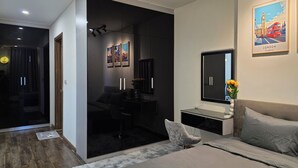 A modern bedroom with a bed, a desk, and a chair. There are framed pictures on the wall and a painting of London.