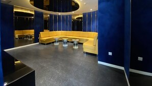 A modern lobby with a curved yellow sofa, round tables, and blue walls.