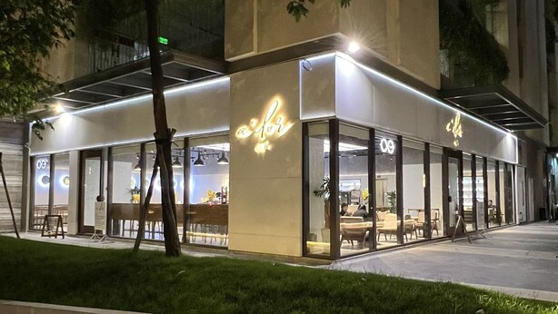 An outdoor cafe with a modern design, featuring a glass facade and outdoor seating.