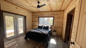 A wooden cabin bedroom with a bed, a ceiling fan, and a window. - Hochabel Hotel (Idabel)